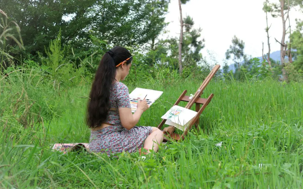 A young woman sketching outdoors in nature, surrounded by greenery, enjoying a peaceful and artistic moment.