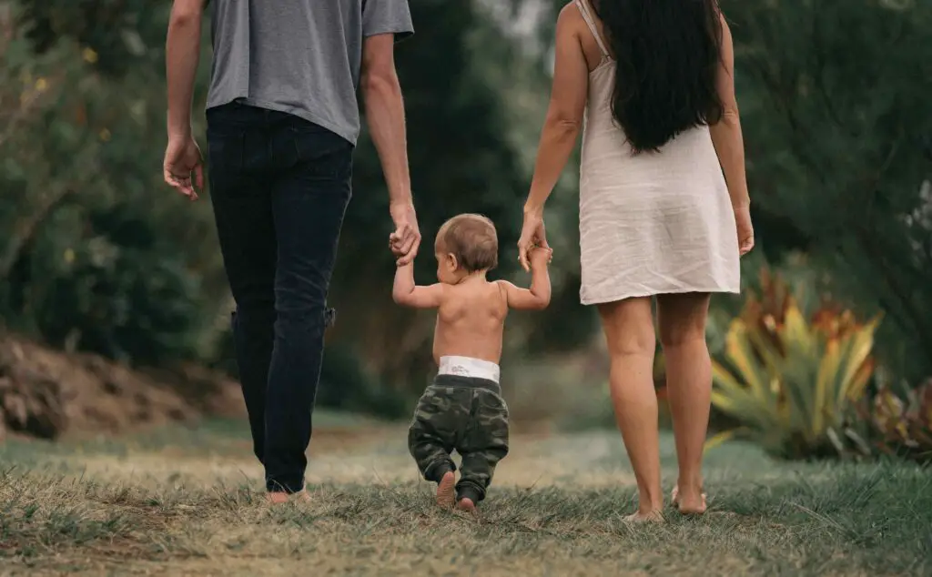 Family-Friendly Activities and Unique Traditions: Things to Do in NYC Labor Day Weekend Parents walking hand-in-hand with their child through a lively park in NYC during Labor Day weekend, surrounded by greenery and local festivities.