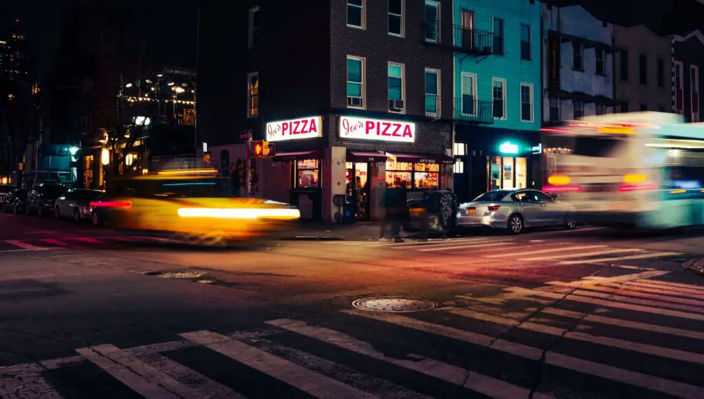 Brooklyn streets at night glowing with warm lights, quiet corners, and the silhouette of the Manhattan skyline in the distance.