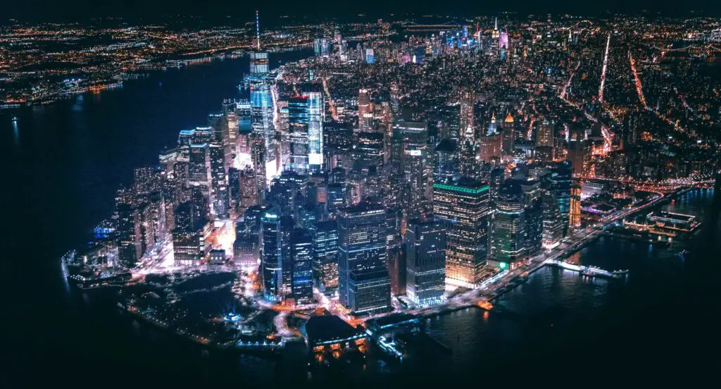 Aerial night view of New York City glowing with lights, highlighting the skyline and lively streets below.
