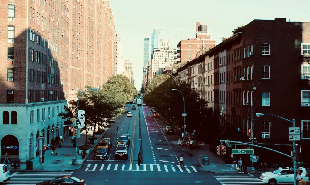 Wide street in the Lower East Side of NYC lined with historic buildings, street art, and a mix of old and new storefronts.