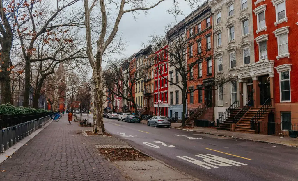 A narrow street in East Village, NYC during autumn, with colorful leaves, cozy cafés, and historic buildings lining the sidewalk.