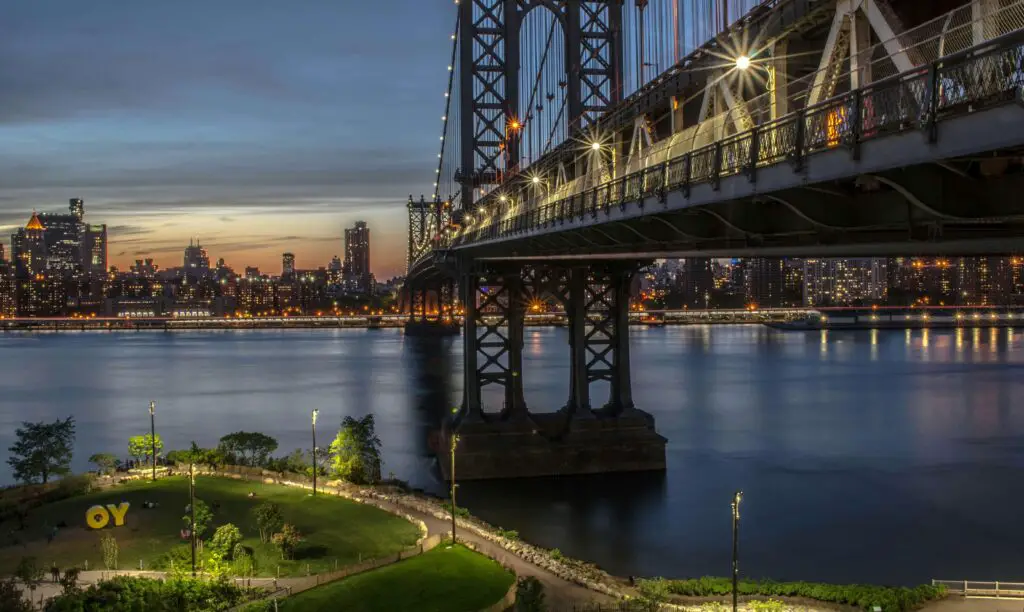 Peaceful view of Roosevelt Island beneath the Queensboro Bridge, with the East River and Manhattan skyline in the background.