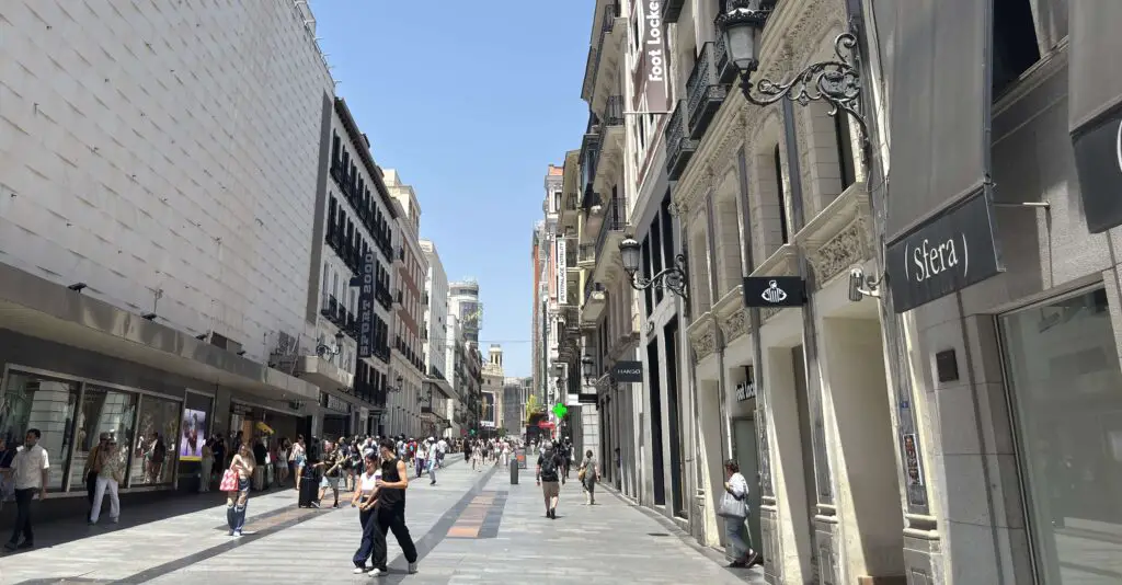 Enjoy Madrid Without Spending a Euro: Free Things to Do in the City Sunny daytime view of Calle Preciados in Madrid, filled with people walking, shopping, and enjoying the lively atmosphere.