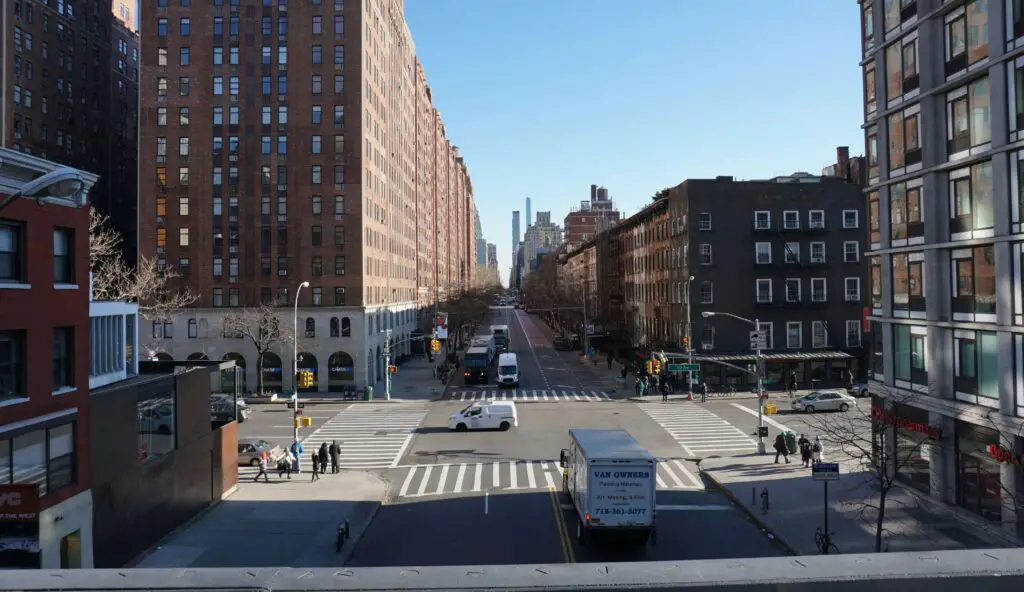 Wide street view in Greenpoint, Brooklyn, lined with local shops, trees, and brownstone buildings on a sunny day.