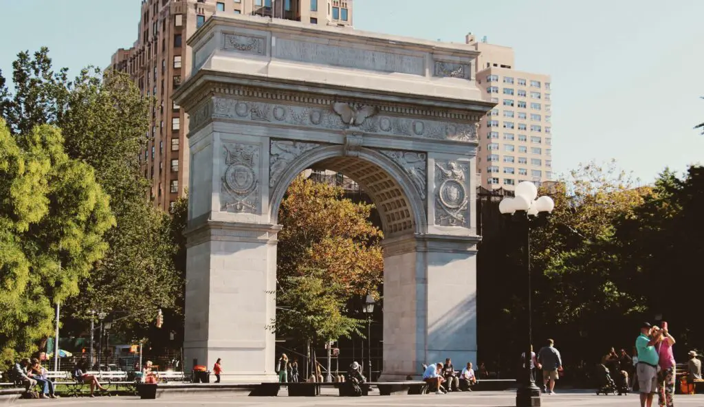 Historic stone arch monument in Greenwich Village, surrounded by trees and tourists enjoying the sunny day.