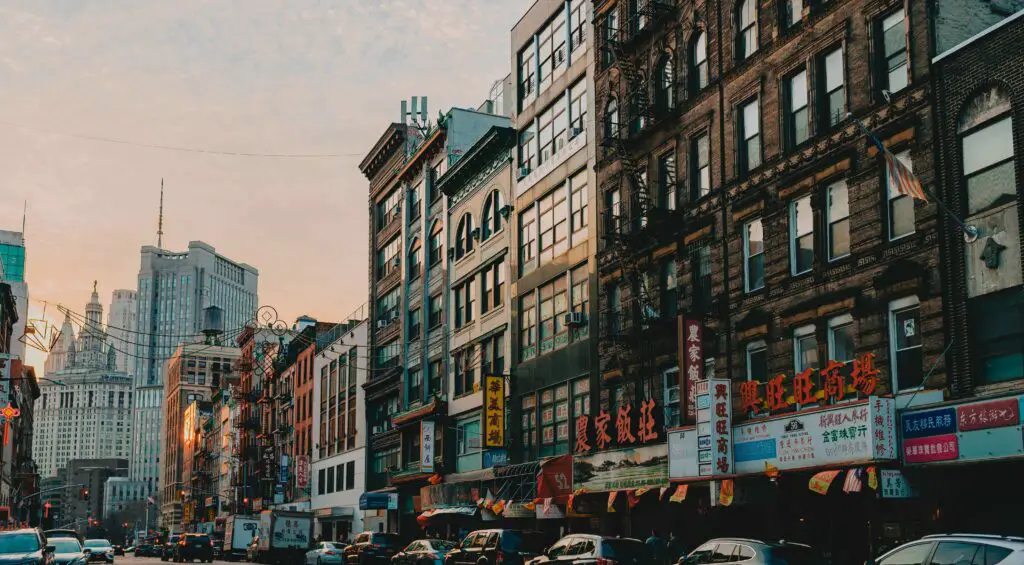 Street view of Chinatown NYC with traditional Chinese lanterns, storefront signs in Chinese characters, and people walking through the lively neighborhood.