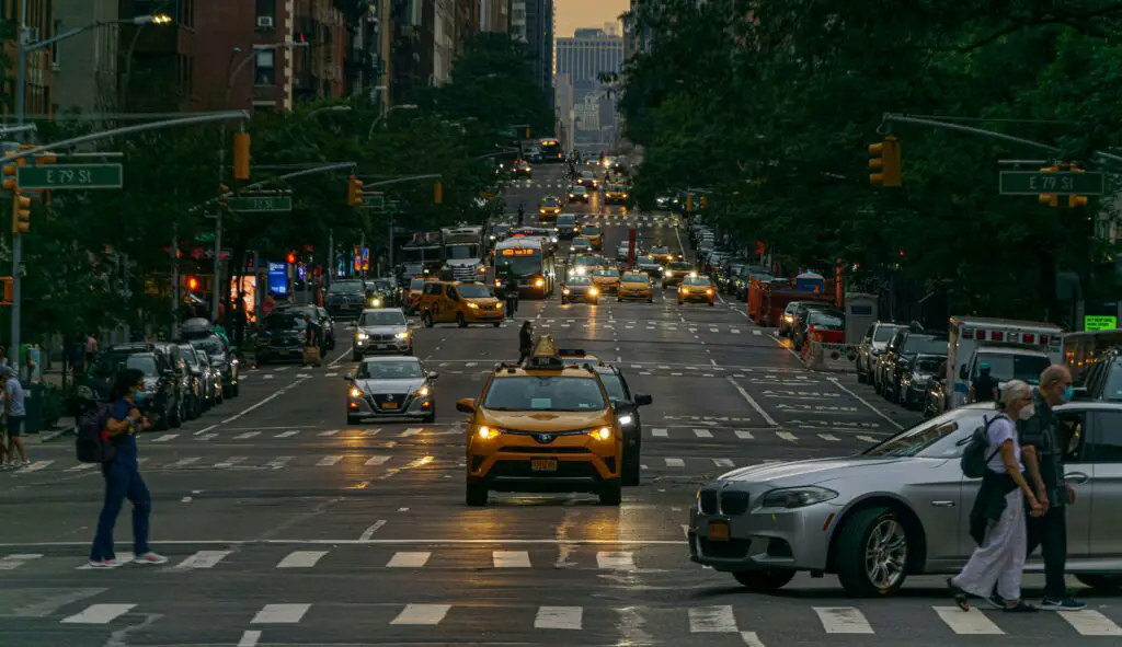 Wide city street in the Upper East Side with a traffic light and people crossing the road on a sunny day.